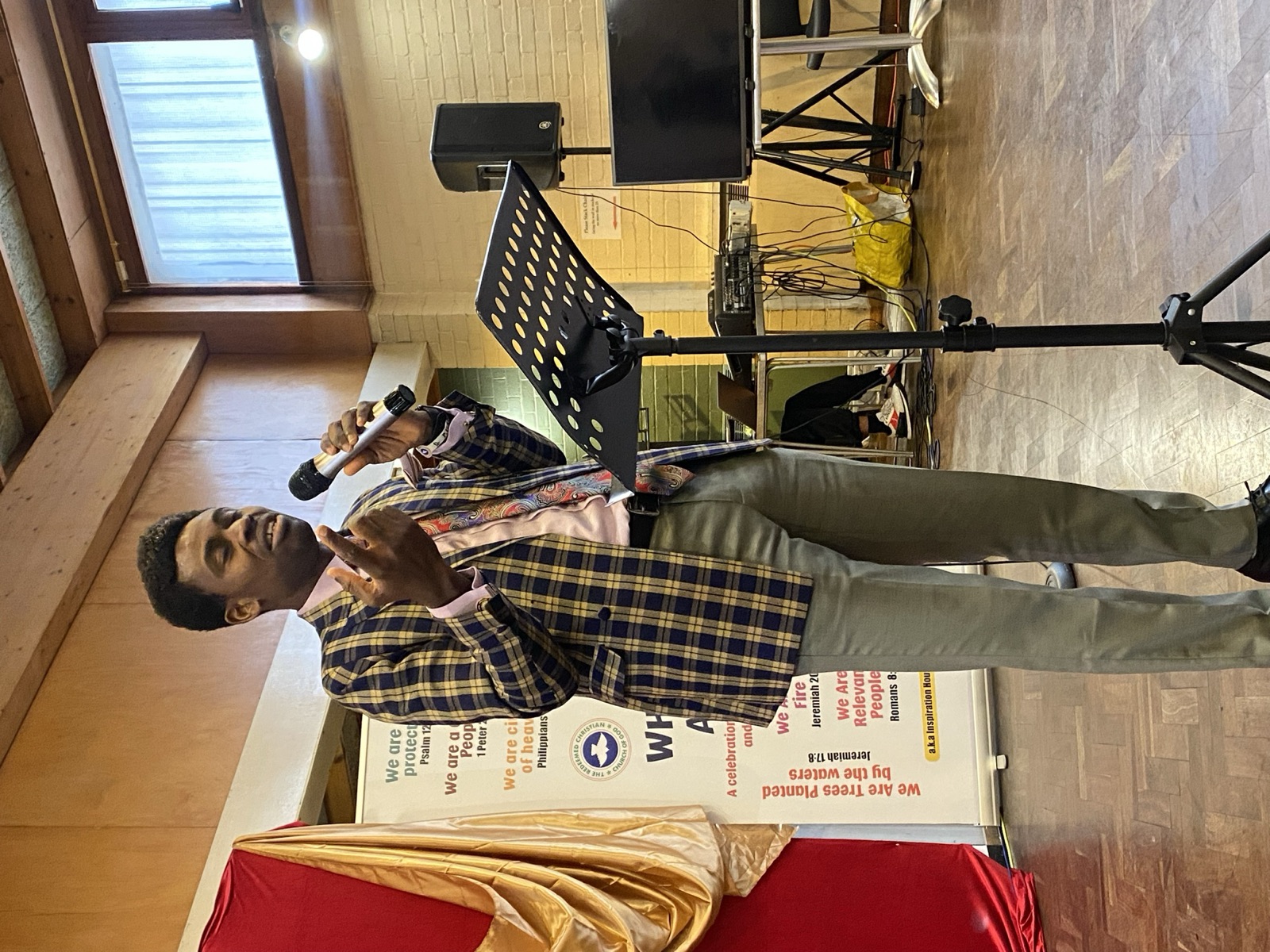 A preacher in a checked blazer speaking with a microphone