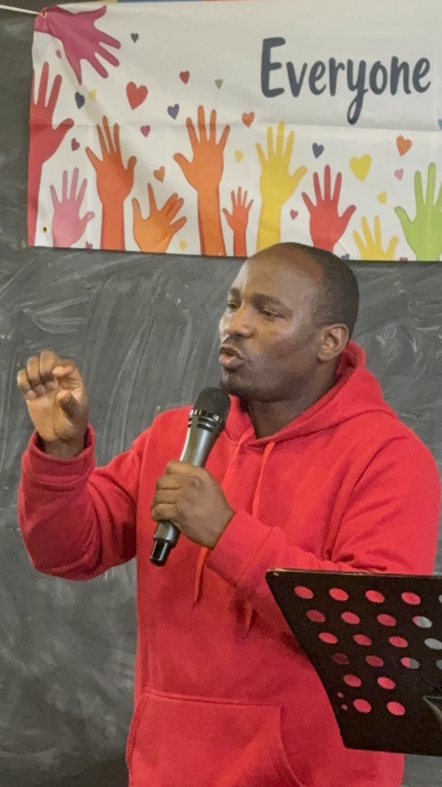 A preacher in a red hoodie speaking into a microphone