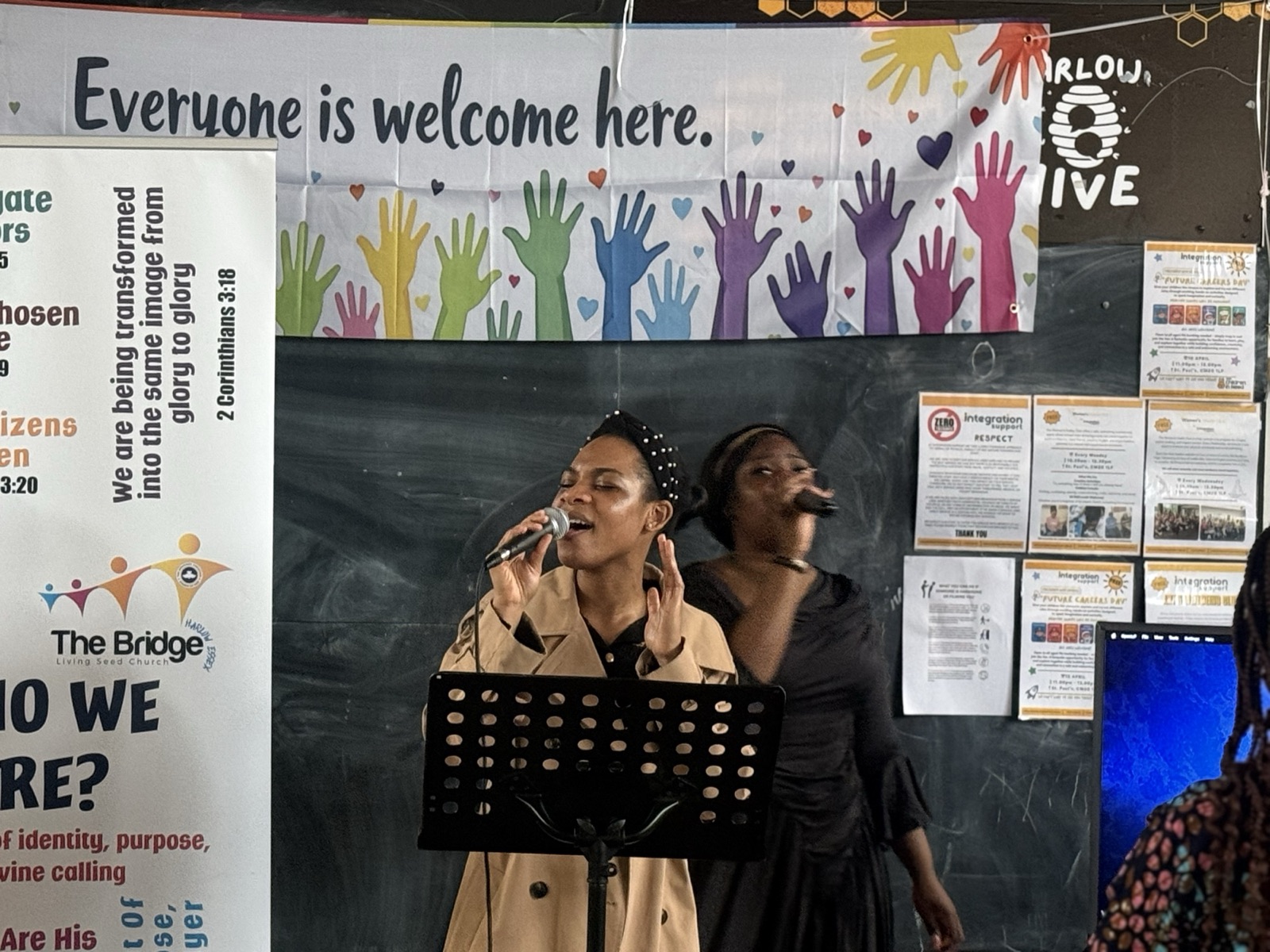 Two singers in front of an 'Everyone is welcome here' banner
